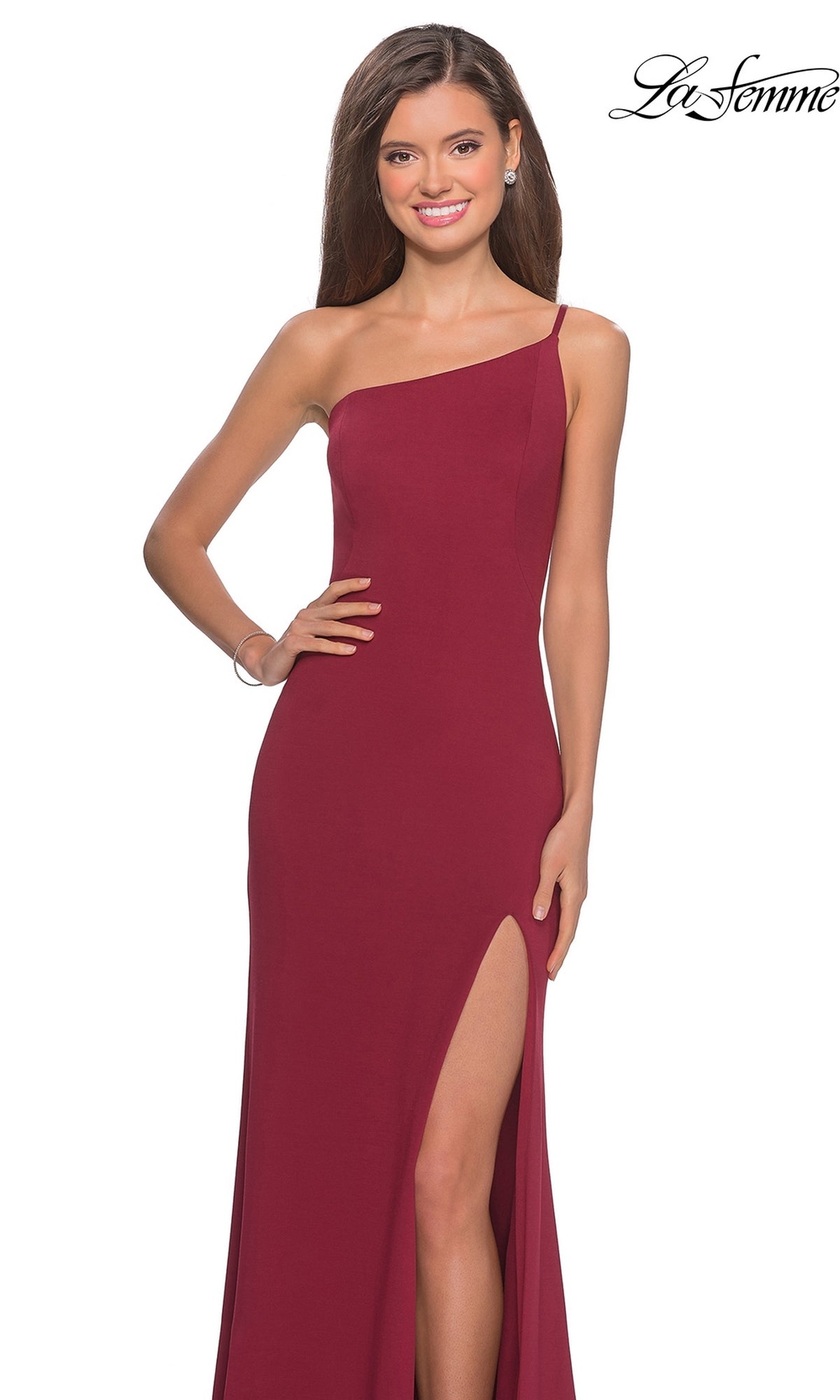A woman confidently poses in the La Femme One-Shoulder Long Formal Dress 28176, a sleeveless burgundy gown with a thigh-high slit, smiling with one hand on her hip against a white background.